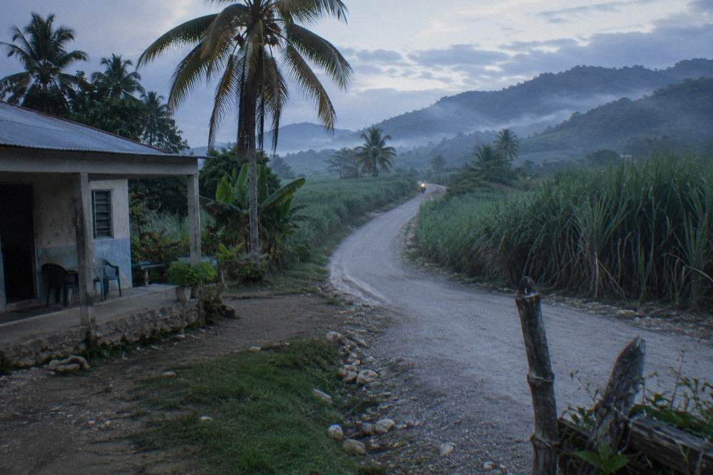 Country road winding through green hills toward a low mountain ridge in the early morning