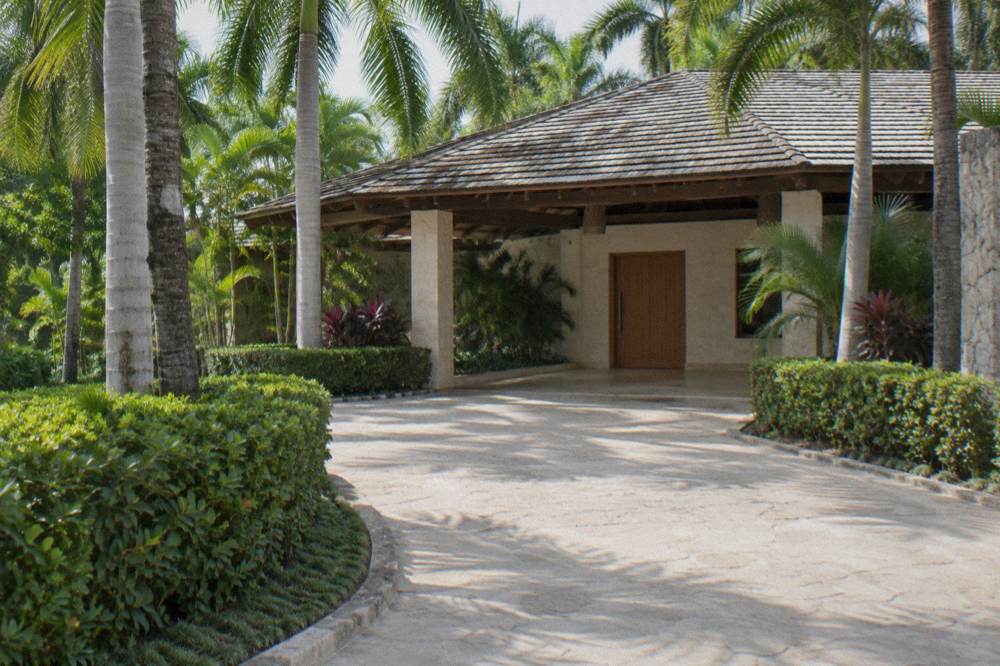 Quiet resort driveway with pale paving, trimmed hedges, royal palms and a closed wooden door