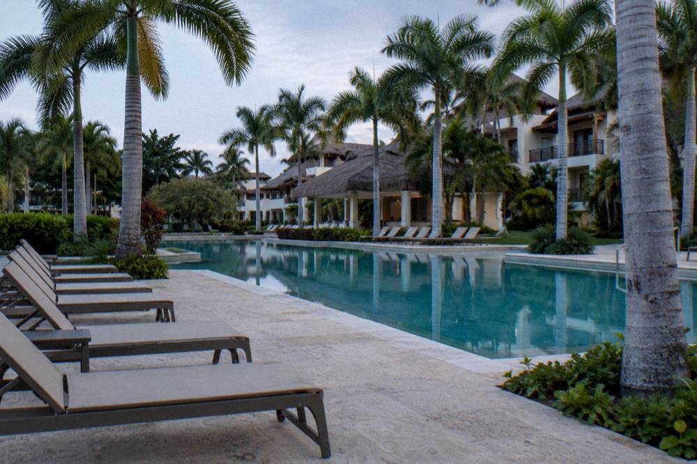 Still resort pool at dawn between royal palms with loungers lined on swept coral stone pavers