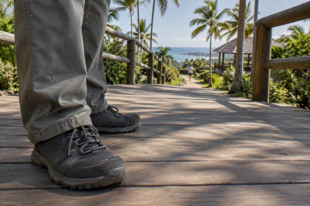 Closed walking shoes and trouser cuffs on a wooden park walkway striped by dappled palm shade