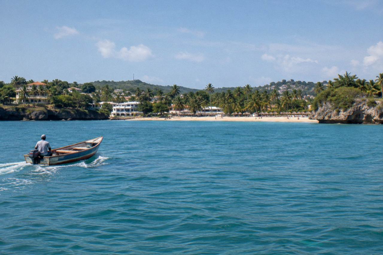 Curved sandy beach with clear turquoise water, palm trees and a green headland at Sosua, Dominican Republic