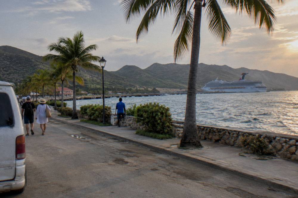 Warm sunset light on tour vans parked in a line along a palm lined seaside road, distant seawall